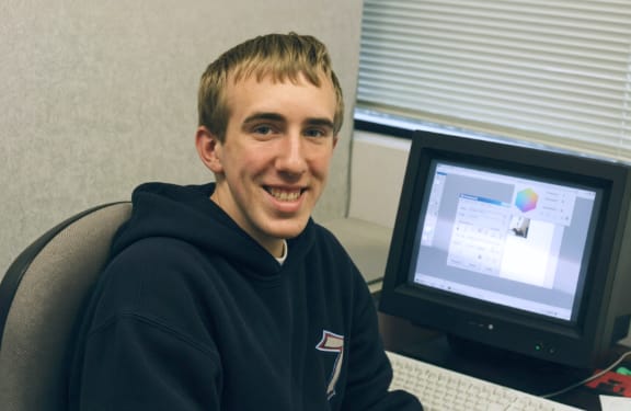 Mike Johnstone seated beside a desktop computer at InfoStar while in high school